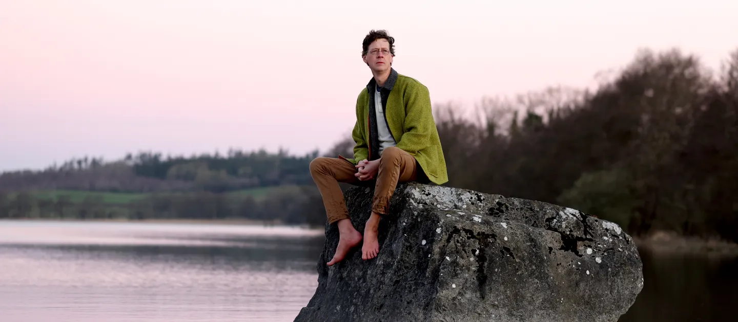 LISTEN TO THE LAND SPEAK still image, magan sitting on a rock over water