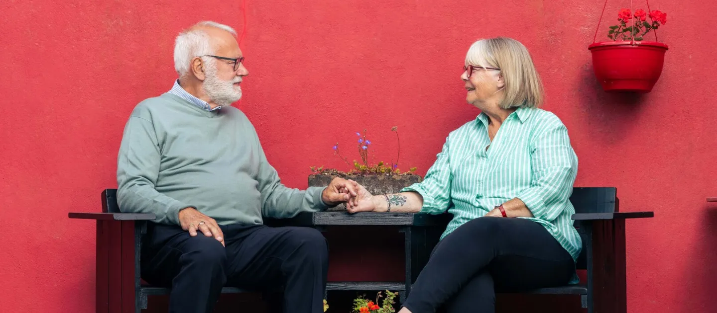 A QUIET LOVE main image, a couple holds hands at a table against a bright red background