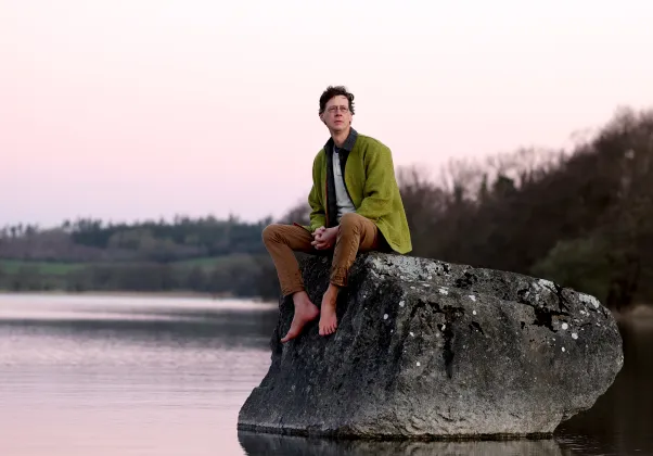 LISTEN TO THE LAND SPEAK still image, magan sitting on a rock over water